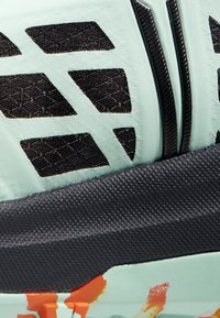 Scarpa atletica verde chiaro con mesh nera e ritagli geometrici, dettagli neri testurizzati e spruzzi di colore sulla suola.