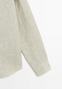 Long sleeve with thin vertical white and beige stripes and a wide cuff on a light background.