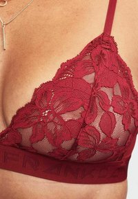 Burgundy lace bralette featuring floral patterns, sheer mesh panels, adjustable straps, and a wide branded band along the bottom.