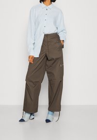 Jasnoniebieska koszula z długimi rękawami, zestawiona z ciemnobrązowymi spodniami cargo z bocznymi kieszeniami i sznurkami u dołu. Niebiesko-białe buty w paski.