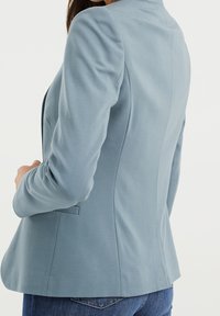 Lichtblauwe blazer met een aansluitend ontwerp, gladde textuur, lange mouwen en subtiele achternaden. Voorzien van een enkele achterzak.