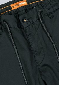 Black shorts featuring an elastic waistband with orange branding, a button closure, and a drawstring. Textured fabric with visible stitching.