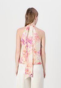 Ermeløs halter-top i myk stoff med blomstermønster i nyanser av rosa og krem. Har en knyttelukking bak og flagrende ender.