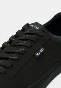 Sneaker nera con materiale superiore liscio, punta tonda, lacci testurizzati e branding HUGO sulla linguetta e sul lato. Design leggero.