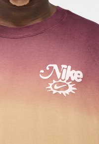 Φούτερ Nike με διαβαθμίσεις από μοβ σε μπεζ, με λευκό λογότυπο και σχέδιο ήλιου. Απαλό, υφασμάτινο με στρογγυλή λαιμόκοψη.