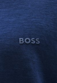 Ναυτικό μπλε ύφασμα με απαλή, υφή επιφάνεια που διαθέτει ένα τρισδιάστατο γκρι λογότυπο "BOSS" το οποίο είναι τοποθετημένο σε εμφανή θέση.