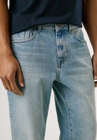 Hellblaue Jeans aus Denim besitzen ein klassisches Design mit geradem Schnitt, sichtbaren Nähten und vorderen Taschen. Der Stoff zeigt eine verblasste Textur.