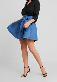 Gonna di jeans con un design svasato, colore blu chiaro, vita con cintura e una texture liscia. Abbinata a sandali neri con cinturini e tacco alto.