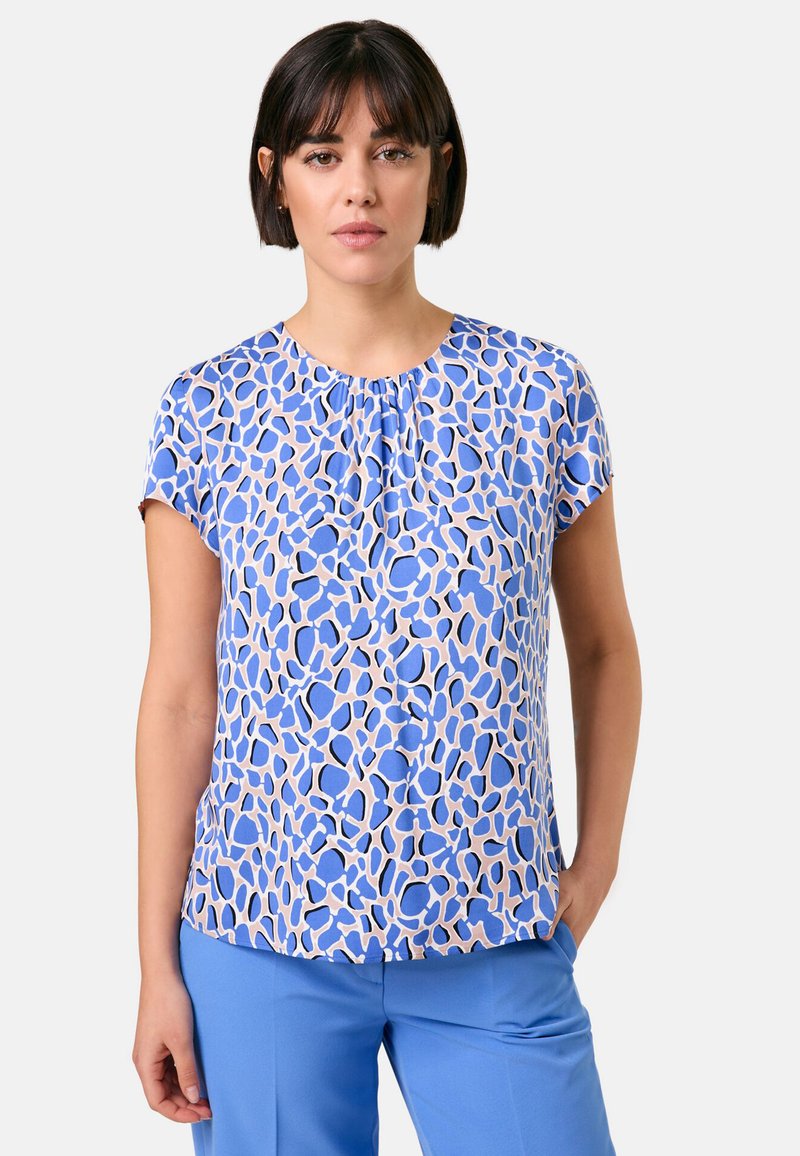 Blaue kurzärmlige Bluse mit einem abstrakten Muster in hellbeige und verschiedenen Blautönen. Weicher Stoff mit rundem Ausschnitt.