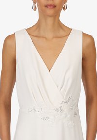 Hvid kjole med dyb V-hals, omslag design og en blonde liv, der har blomster broderi og perle detaljer.