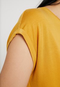 Senapsgul kortärmad topp med en mjuk, ribbad textur och uppvikt ärmdetalj, som visar upp en enkel och modern design.