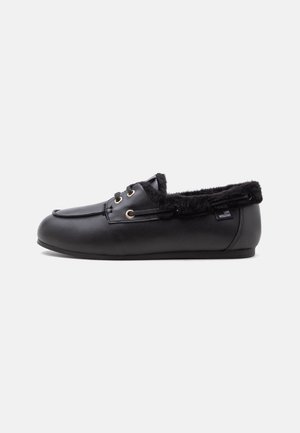Black leather moccasin slipper with black fur lining and gold eyelets, low flat sole, and small "Love Moschino" label on side.