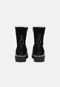 Stivaletti neri in suede con fodera in pelliccia, punta rotonda, chiusura con cerniera e dettagli in pelle. Presentano un tacco robusto e cuciture a contrasto.