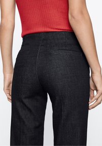 Zwarte denim broek met een rechte snit, voorzien van achterzakken en een soepele textuur. De stof heeft een subtiele glans.