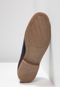 Scarpa in suede nera con suola in gomma tan; presenta una forma arrotondata e un motivo a trama sulla suola.