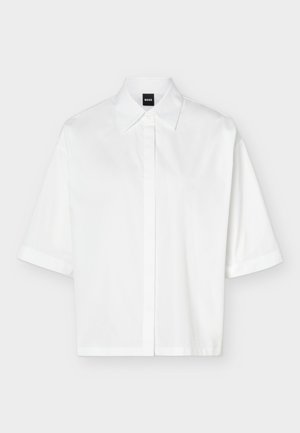 Valkoinen lyhythihainen kauluksellinen paita, jossa on piilotettu nappilista ja musta "BOSS"-merkkikilpi kaula-aukon sisäpuolella.