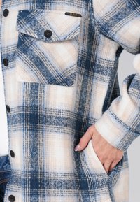 Fleece shirtjack in blauw en crèmekleurig ruitpatroon, met een borstzak, knoopsluiting en een ontspannen pasvorm met zijzakken.
