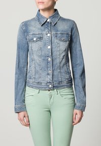 Ljusblå denimjacka med en figursydd design, två bröstfickor, silverfärgad knappar och långa ärmar, tillsammans med mintgröna byxor.