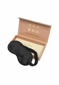 Svart satin sovmask med samlad tygband, placerad ovanpå en krämfärgad, märkeslåda med guldikoner och detaljer.