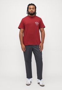Mørkerød bomulds t-shirt med korte ærmer, parret med grå lige bukser. Hvide sneakers skaber kontrast med sorte og blå accenter.