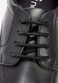 Chaussure habillée en cuir noir avec une finition lisse, un bout rond et six lacets noirs enfilés à travers des œillets. Couture détaillée visible.