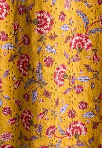 Kollane kangas lillemustriga, kus on punased ja sinised lilled, millel on kogu materjalil väikesed augud.