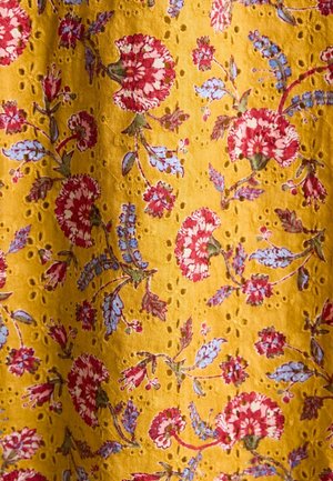 Żółta tkanina z kwiatowym wzorem zawierającym czerwone i niebieskie kwiaty, ozdobiona małymi dziurkami w całym materiale.