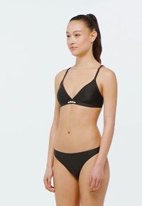 Černý bikini set z hladkého materiálu; trojúhelníkový bralet s tenkými ramínky a logem; odpovídající nízké kalhotky s minimálním pokrytím.
