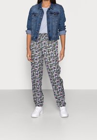 Blå jeansjacka med knappfront och fickor med klaff, matchad med blommönstrade byxor med svart bakgrund och flerfärgade blommor.