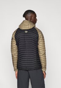 Γιλέκο επενδυμένο με μαύρο κορμό και χακί μανίκια. Διαθέτει κουκούλα, καπιτονέ υφή και λογότυπο στο πίσω μέρος.