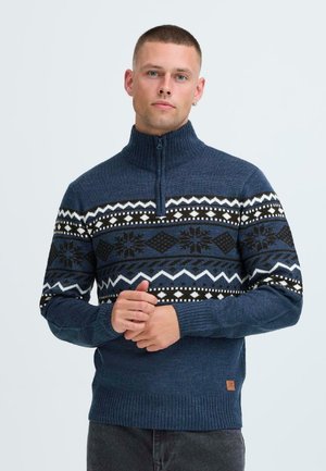 Maglione lavorato a maglia di colore blu scuro con colletto alto con zip, decorato con motivi geometrici e fiocchi di neve in bianco e marrone sul petto.