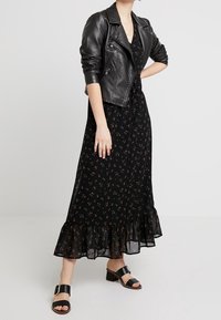 Abito lungo nero a fiori con orlo a balze, indossato sotto una giacca di pelle nera cropped da biker. Completato con sandali neri con tacco a blocco.