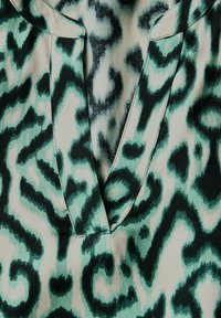 Un tessuto a stampa leopardata verde e nera presenta un décolleté a V e una texture liscia, evidenziando motivi fluidi e colori in contrasto.
