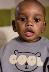 Sweatshirt gris avec un design d'ours et le mot "COOL" en lettres crémeuses duveteuses, présentant un col rond et des boutons-pression aux épaules.