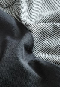 Striktekstil med et grå sektion og et lysegrå mønster med sorte striber; glat tekstur, blødt stof.