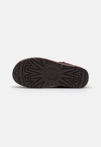 Brown rubber outsole with a textured pattern, featuring zigzag grooves and a central circular logo. Designed for enhanced grip and durability.