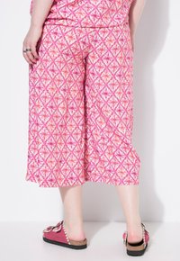 Roze culottes met een geometrisch patroon, voorzien van een elastische tailleband en een relaxte fit. Gecombineerd met roze instapper sandalen.