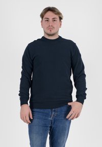 Felpa girocollo blu navy, realizzata in tessuto morbido, con maniche lunghe e polsini a coste, abbinata a jeans di denim blu.