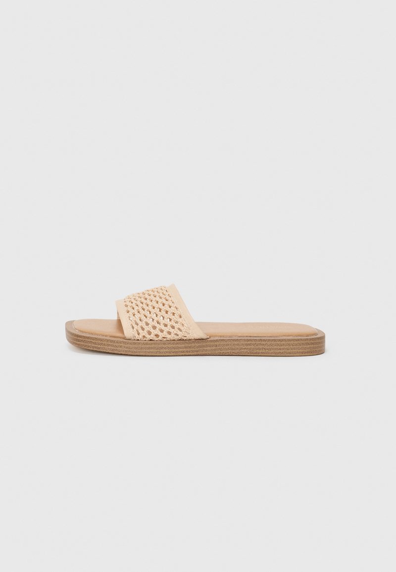 Sandal de slide em bege claro com parte superior trançada, sola plana e uma palmilha lisa em tom de marrom. Design simples, sem hardware ou enfeites adicionais.