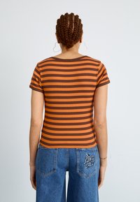 Débardeur à manches courtes rayé en orange et marron, à texture côtelée, avec un col rond et une coupe ajustée, associé à un pantalon en denim bleu.