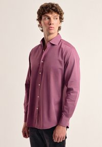 Camisa de manga larga y con botones en un color lila sólido. Presenta un cuello clásico, un logo sutil en el pecho y un dobladillo recto.