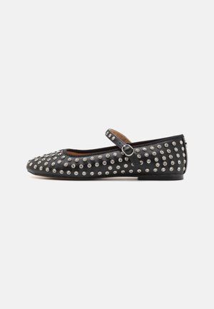 Black flat shoe with rounded toe, adorned with silver studs. Features a single strap with a buckle and a low heel. Smooth leather texture.