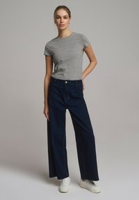 Szara koszulka z krótkim rękawem w połączeniu z szerokimi ciemnoniebieskimi dżinsami. Białe sneakersy dopełniają stylizację. Prosty design z minimalnymi akcentami.