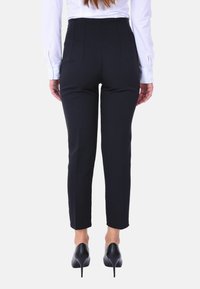 Pantaloni neri sartoriali con una vestibilità slim e vita alta, caratterizzati da cuciture verticali, indossati con una camicia bianca e tacchi neri.