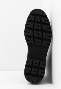 Semelle de chaussure en caoutchouc noir, avec un motif de bande de roulement texturé pour adhérence. Taille indiquée : 37. Design plat sans éléments métalliques ni accents visibles.