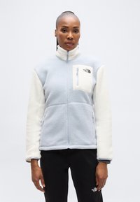 Ανοιχτό μπλε φλις μπουφάν με κρεμ μανίκια, φερμουάρ μπροστά, ψηλό γιακά και τσέπη στο στήθος με φερμουάρ που φέρει λογότυπο. Μαλακή υφή, άνετη εφαρμογή.