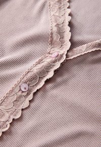 Hele roosa soonikuga kangas pitsäärisega kaelusel. Kaks roosat nööpi lisavad disainile õrna detaili.