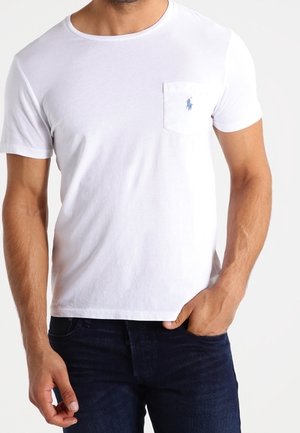 Camiseta de algodón blanca con cuello redondo y mangas cortas, que presenta un pequeño logo azul en el bolsillo del pecho izquierdo.