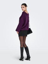 Maglione viola lavorato a maglia con una vestibilità ampia e maniche larghe, abbinato a una mini gonna nera e stivali in pelle neri alti fino al ginocchio.