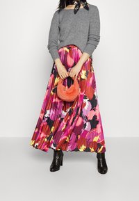 Grijze trui, kleurrijke geplooide rok met bloemmotieven in roze, oranje en geel, gecombineerd met een kleine oranje pluizige handtas en zwarte laarzen.